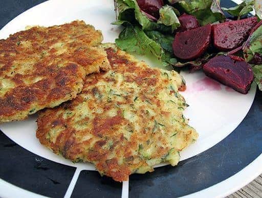 Crispy and crunchy Fried Zucchini Cakes in white plate with beet salad on side