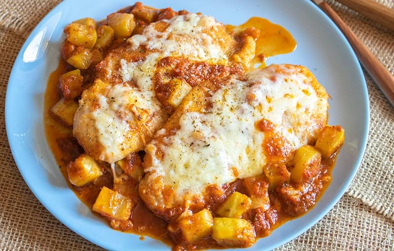 a plate of Chicken Parmigiana with sauce and vegetables