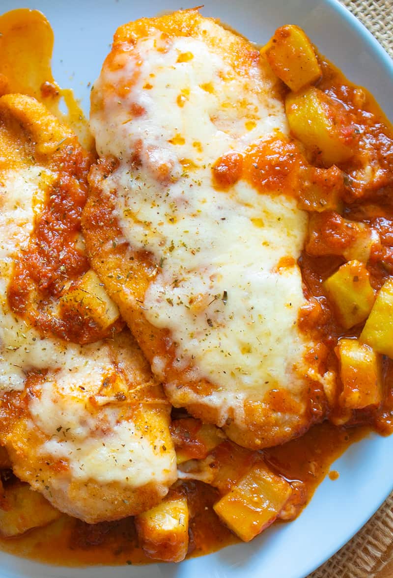 close up plate of Chicken Parmigiana with sauce and vegetables