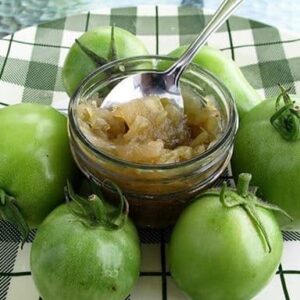 a cup of Green Tomato Relish around 6 pieces of fresh green tomatoes on a checkered green plate