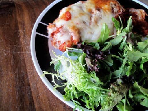 A plate with Chicken Parmigiana and vegetable salad on side