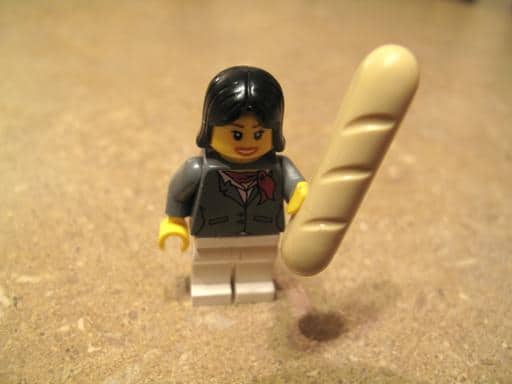 lego holding a gigantic baguette and wearing a coat with the zippy little scarf around her neck
