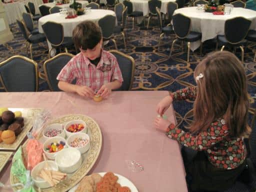 two kids decorating their cupcakes in the table of cupcakes and sprinkles