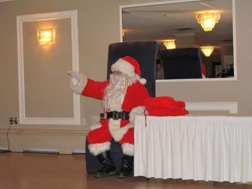 human Santa sitting in a black chair near the table with a big mirror on his background