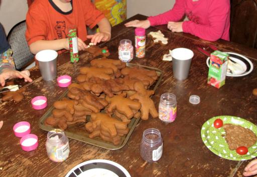 Gingerbread cookies in a tray at the middle of the table, icing and sprinkles on the sides