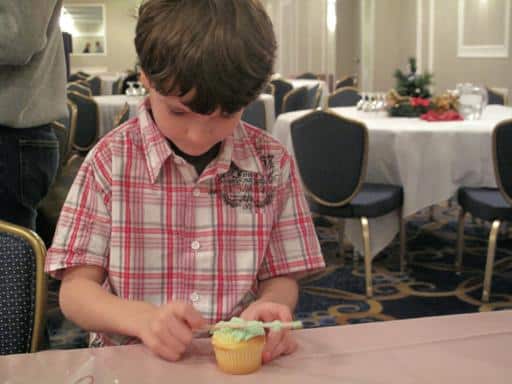 little boy spreading icing on top of his cupcake