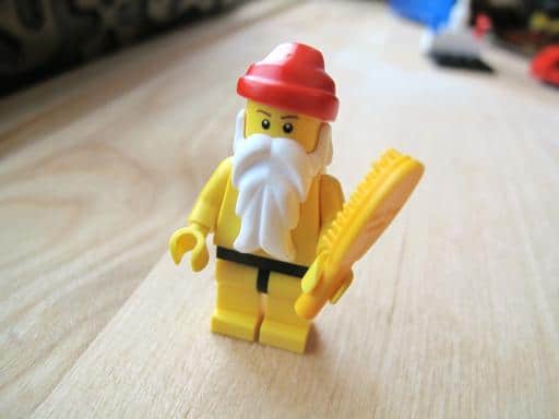 yellow lego Santa with white long beard holding a yellow hair brush 