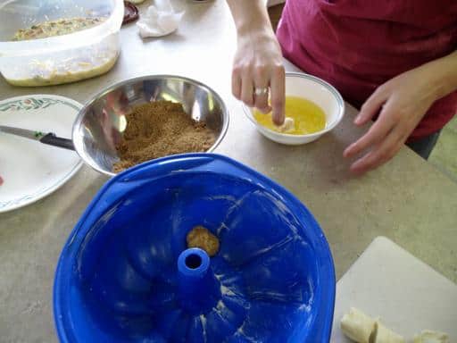 Dipping monkey bread dough into butter, then sugar, then placing in a bundt pan