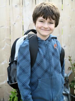 close up of a young boy wearing blue jacket with his backpack 