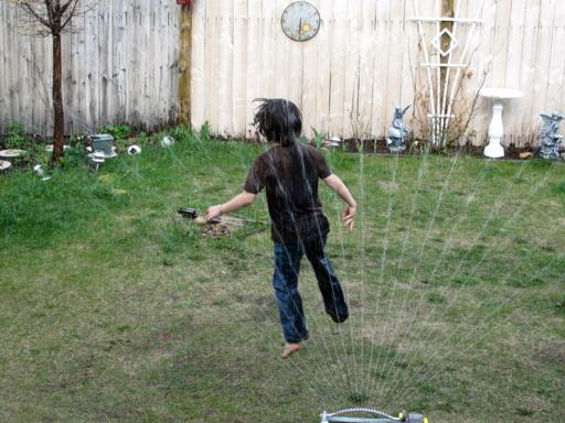 young boy playing on the water from hose in the lawn