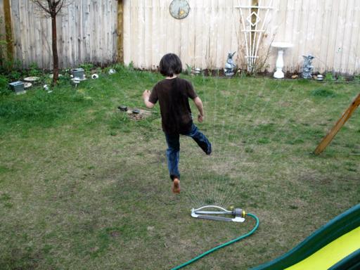 young boy playing on the water from hose in the lawn