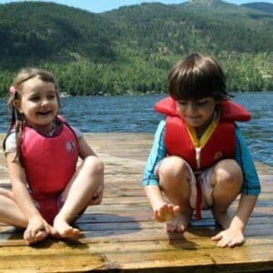 kids wearing red life jackets sitting in the wood ramp in the lake