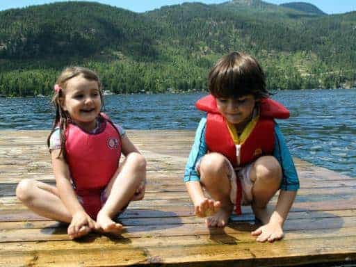 kids wearing red life jackets sitting in the dock in the lake