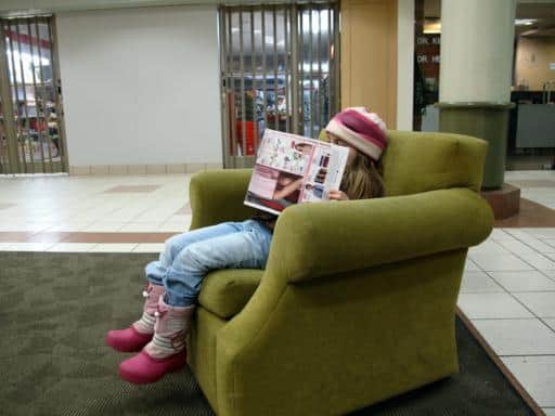 little girl sitting in the couch, reading magazine