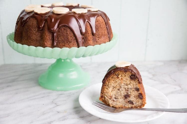 Chocolate Banana Buttermilk Bundt Cake in a jade green cake holder and a slice in a white plate with fork