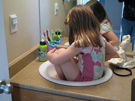 little girl sitting in the sink of the bathroom