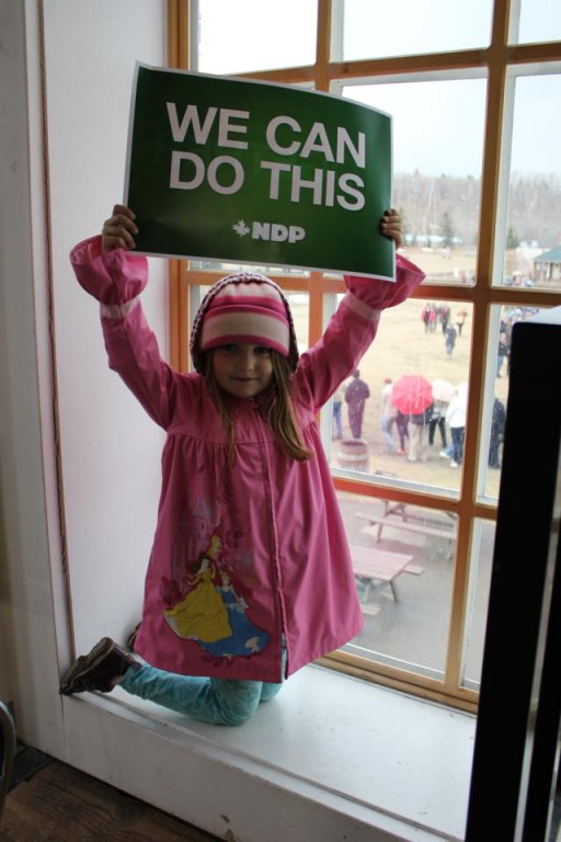 little girl standing near the window holding a green sign