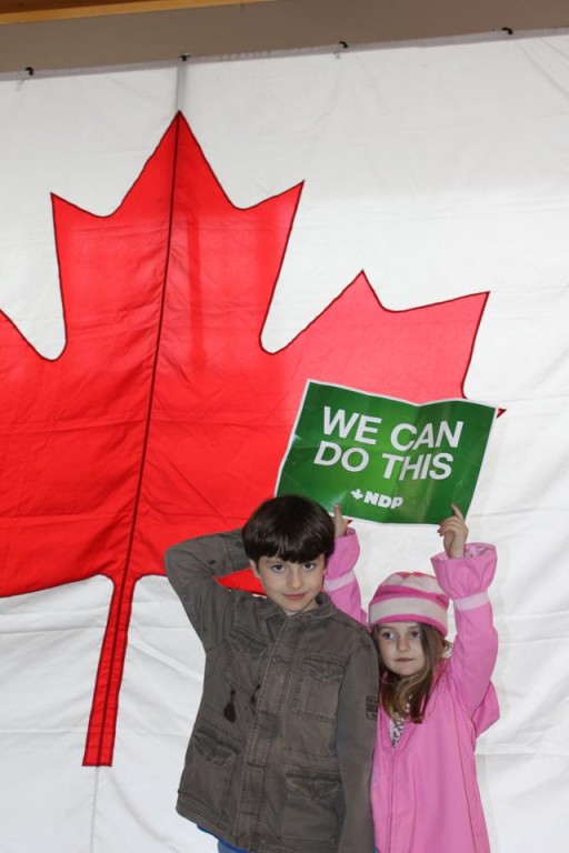 two kids waving a green sign with the Canadian flag on their background