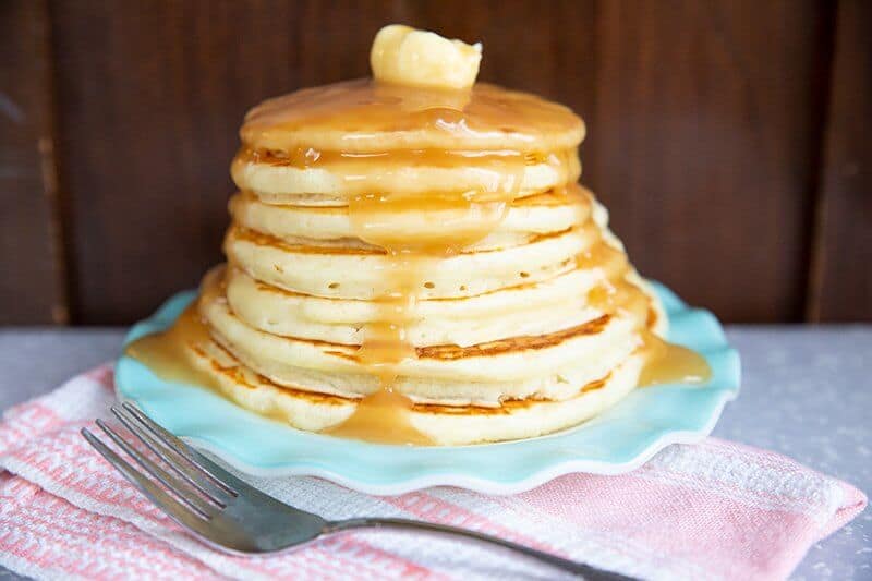 stack of Buttermilk Pancakes topped with butter and syrup in a ruffled dessert plate