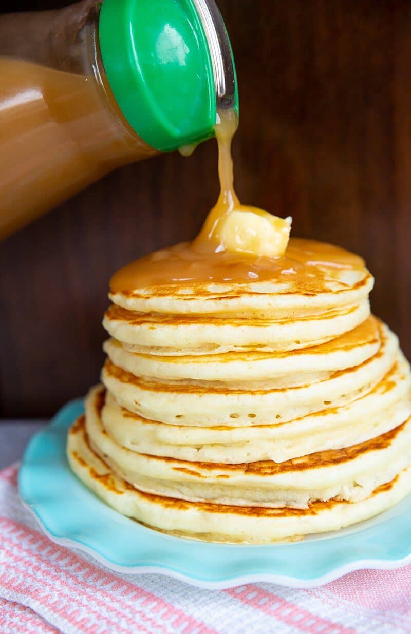 adding syrup from a pitcher to a stack of Buttermilk Pancakes
