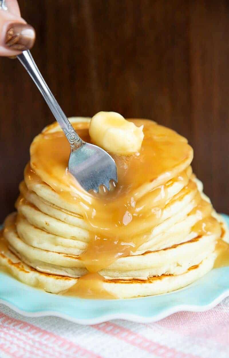 a fork in a stack of Buttermilk Pancakes topped with butter and syrup in a ruffled dessert plate