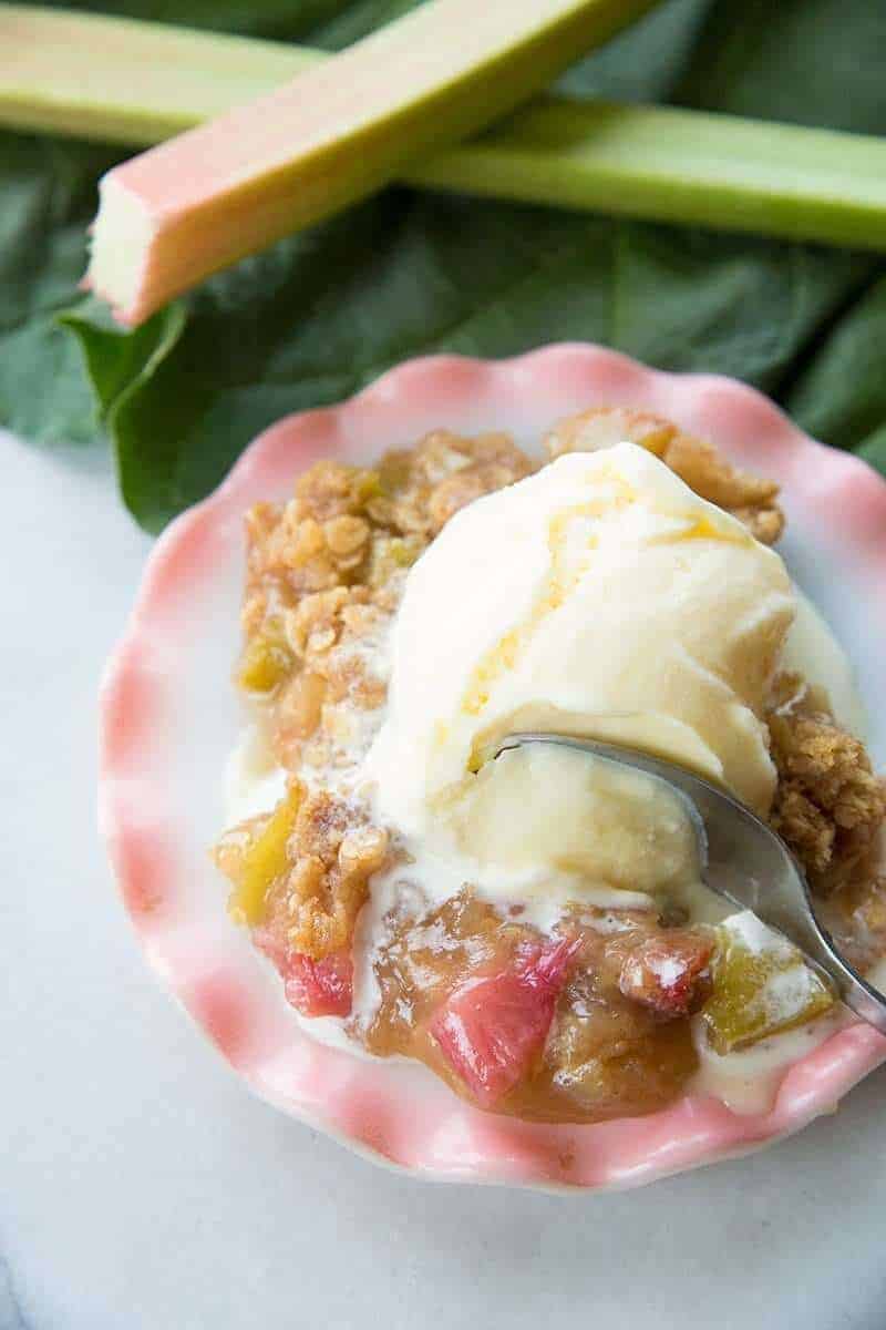 Close up of rhubarb crisp & vanilla ice cream with a spoon digging into it
