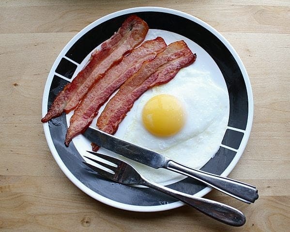 fried Duck Eggs and bacon strips in a plate with fork and knife on wood background