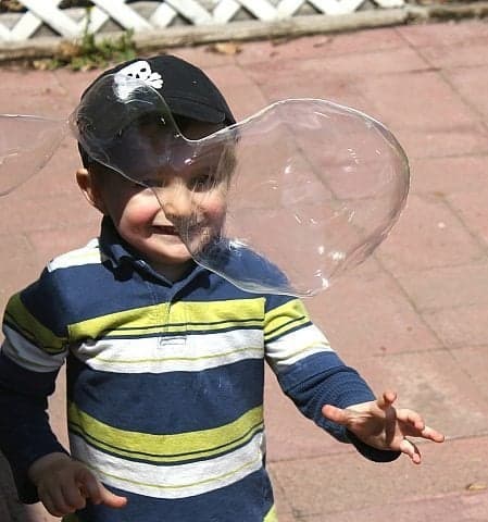 close up of a kid and a giant bubble in front oh him