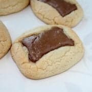 A close-up of soft, golden cookies from a classic chocolate chip cookie recipe, each topped with a melted piece of chocolate and arranged on a white plate with a subtle leaf pattern.
