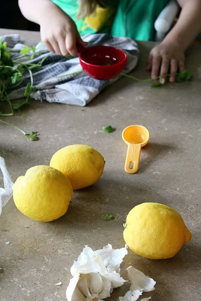 ingredients in making Lemon Cilantro Roast Chicken on the table with a child holding a red measuring spoon