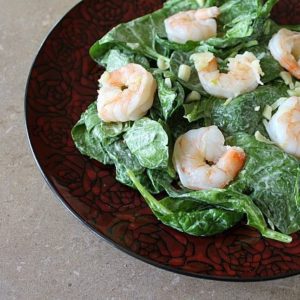 red rose designed plate with greens and dressing topped with steaming hot shrimp