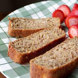 3 slices of Buttermilk Banana Bread in a green checkered plate with some fresh strawberries