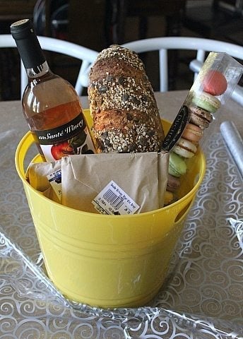 big yellow bucket with En Sante's Rhubarb wine, Duchess macarons, a gift package, Sylvan Cheese's Old Grizzly and a loaf of pumpkin sourdough