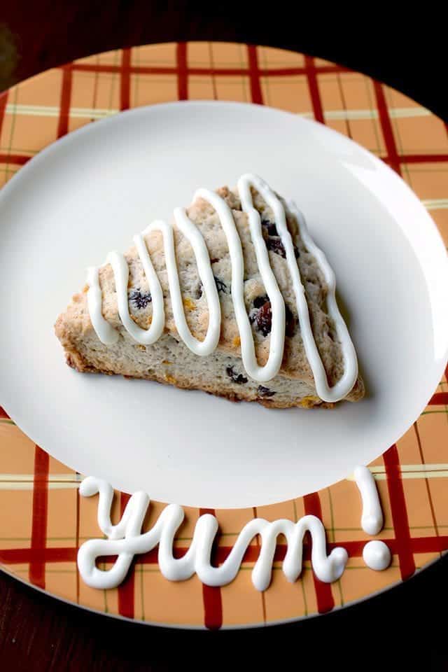 top down shot of Simple Carrot Cake Scones in a white plate, drizzled with tangy cream cheese icing with a "YUM" word