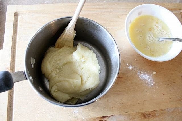 Choux Pastry Dough in a Pot and beaten eggs in a white bowl