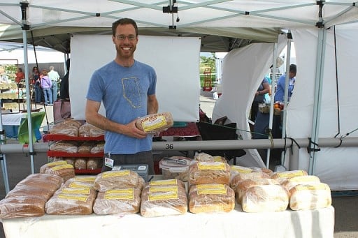 man holding a packed loaf of cinnamon raisin bread, standing in their booth