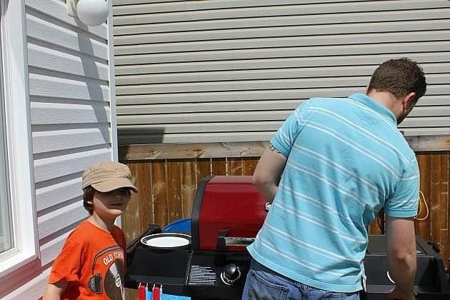 Dad lighting the fires of BBQ machine with a little boy on his side