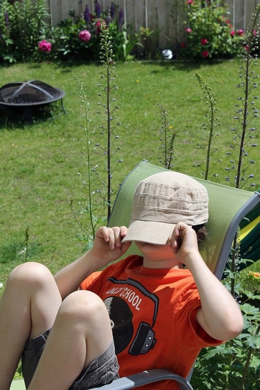 little boy covering his face with his cap while sitting in a camping chair