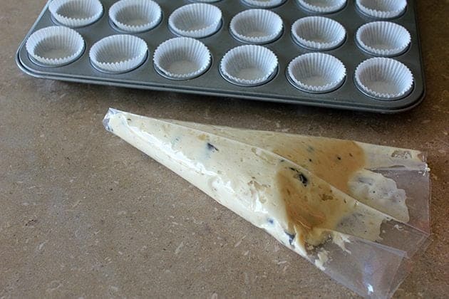 mini muffin tins lined with white paper liners, a plastic icing bag with mixed batter