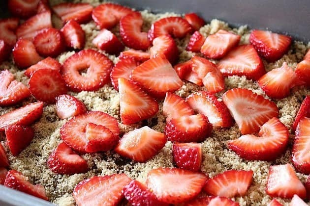 baking pan with sprinkled brown sugar on melted butter and chopped strawberries on top