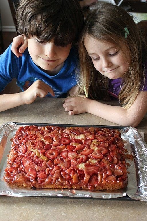 child staring at the freshly baked Strawberry Rhubarb Upside Down Cake in a pan