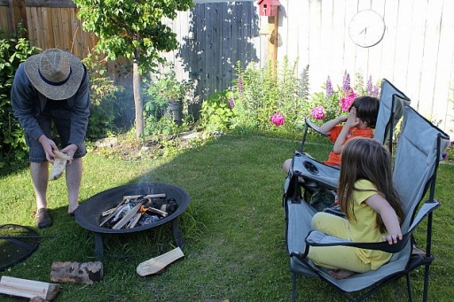 setting up the fire at the backyard with two kids sitting on camping chairs