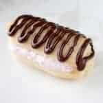 A small éclair with pink cream filling and a drizzle of chocolate icing on top sits on a white plate.