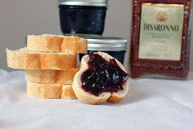 A stack of toast bread slices, one with boozy sweet cherry preserves spread over it. Small jar containers with cherry preserved on the background.
