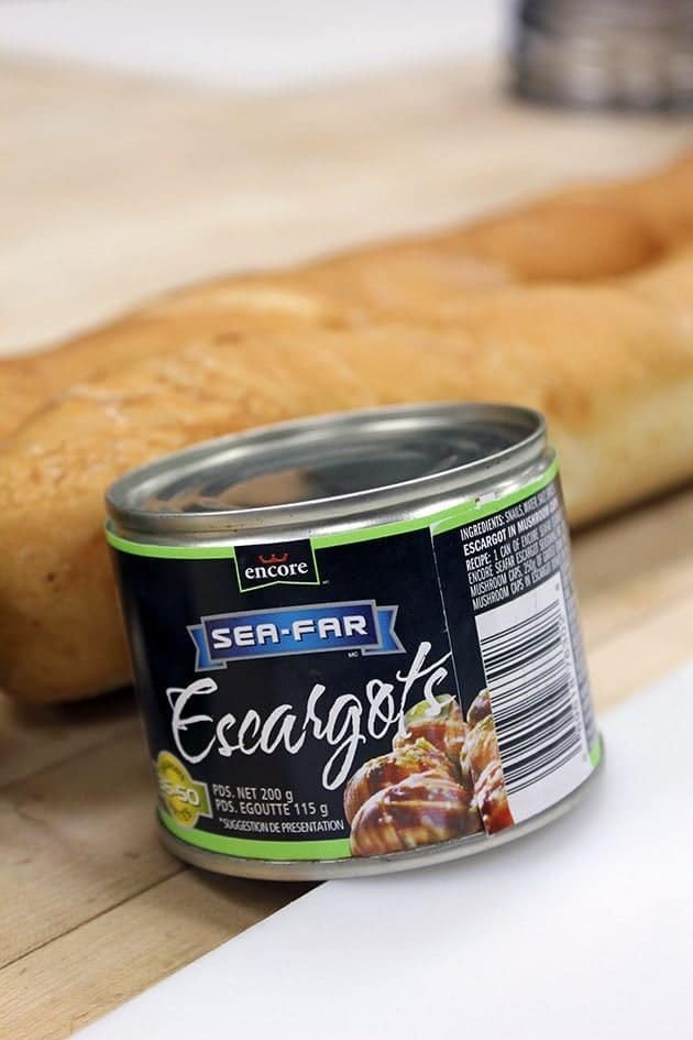 small can of escargots with french bread on background