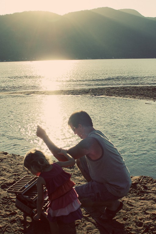 a man and his little girl near the lake during the sunset