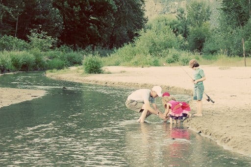 kids fishing at the side of a lake with their grandfather