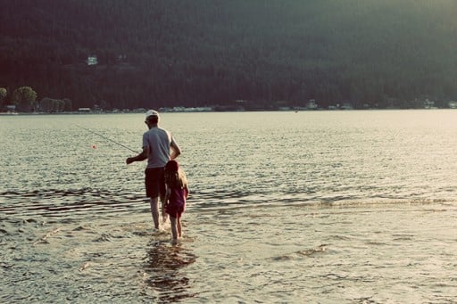 grandfather and little girl walking in the lake with the fishing rod