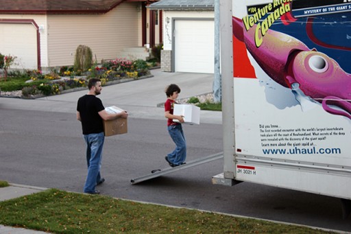 a man and a kid carrying boxes to the truck van