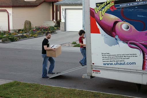 a man and a kid carrying boxes entering the truck van